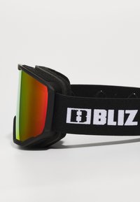 Lunettes de ski avec une large lentille réfléchissante en dégradé rouge et vert, monture noire avec un rembourrage doux et une sangle noire avec logo.