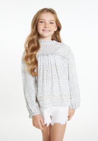 Lyseblå bluse med blomsterprint, lange ærmer, samlingdetaljer og en flæse i halsen, parret med hvide shorts.