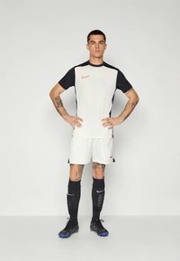 Biała koszulka piłkarska Nike z czarnymi rękawami, w zestawieniu z białymi szortami, czarnymi skarpetkami i butami. Posiada małe czerwone logo Nike na piersi.