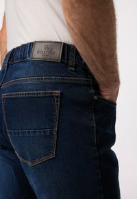 Tmavě modré džíny z denimu s elastickým pasem, s koženou nášivkou, oranžovým prošíváním a designem zadní kapsy.