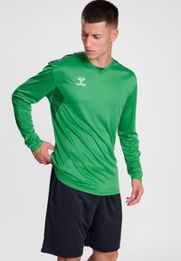 Langsleeve groene sportshirt met een V-hals en zwarte accenten, gecombineerd met zwarte shorts. Gemaakt van een gladde, rekbare stof. Hummel-logo weergegeven.