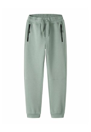 Pantalon de survêtement vert clair avec taille élastique, cordon de serrage, deux poches avant zippées avec fermetures éclair noires et chevilles côtelées.