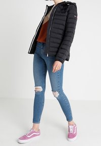 Černá péřová bunda se zipem, svetr s barevným blokem v hnědé a krémové barvě, modré potrhané skinny džíny a růžové semišové tenisky s bílou podrážkou.