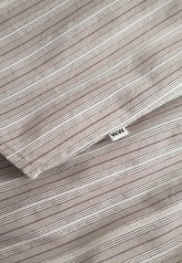 Țesătură din in striat în taupe cu linii albe și gri. Prezintă o etichetă mică țesută cu "W.W." într-un colț. Textură netedă.