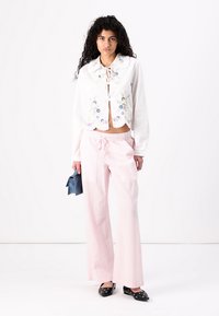 Weißes, bauchfreies Bluse mit floralen Stickereien und Rüschensaum; hochgeschnittene rosa karierte Hose; schwarze spitze Schuhe.