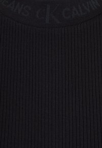 Czarna materiał o żebrowanej fakturze z teksturowanym wzorem. Pas ma wytłoczone logo, co wpływa na dopasowany kształt i odczucie.