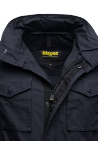 Ciemnoniebieska kurtka z wysokim kołnierzem, z zamkiem błyskawicznym i zatrzaskiem, dwoma przednimi kieszeniami oraz metką informującą o rozmiarze M.