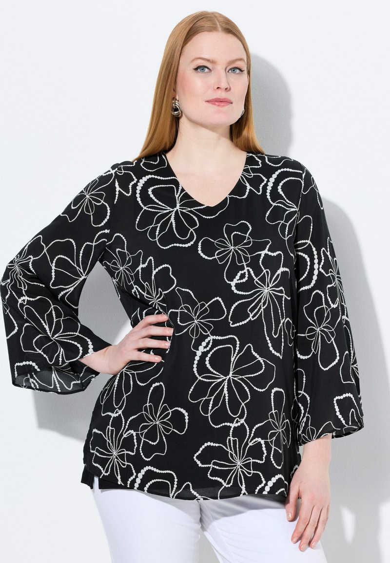 Blusa nera con motivo floreale bianco, con scollatura a V, maniche lunghe e vestibilità leggermente ampia. Il tessuto testurizzato esalta i dettagli visivi.