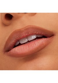 Zbliżenie ust z matową, nude szminką, ukazujące gładką teksturę i delikatne kontury. Zęby są białe i widoczne.