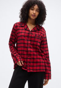 Κόκκινο και μαύρο πουκαμισό φανέλας καρώ με γιακά, κουμπιά μπροστά και τσέπη στο στήθος. Μακριά μανίκια με λεπτομέρειες μανσετών. Απαλή υφή.