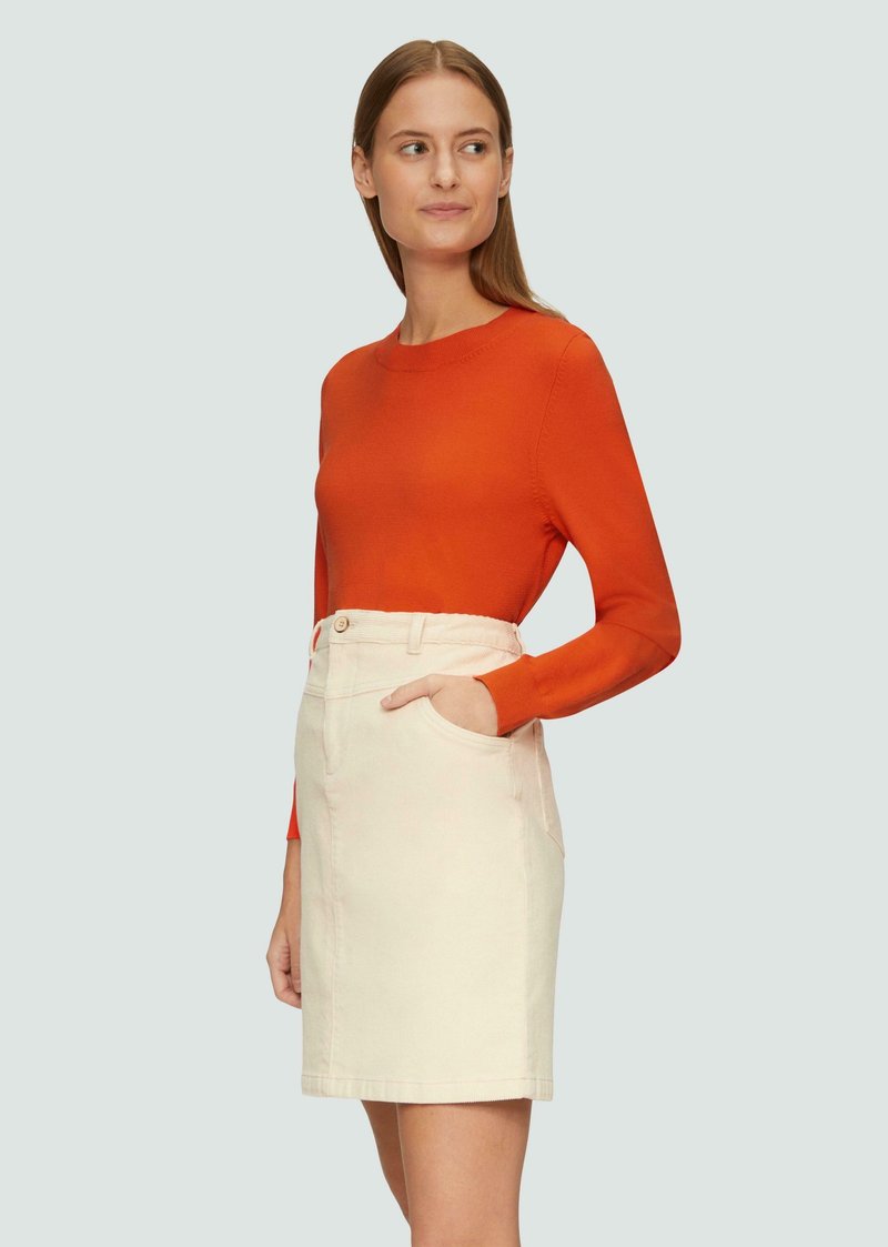 Pomarańczowy sweter z długim rękawem, w zestawie z kremową spódnicą dżinsową zawierającą boczne kieszenie i zapięcie na guziki z przodu, prezentowany na jasnym tle.