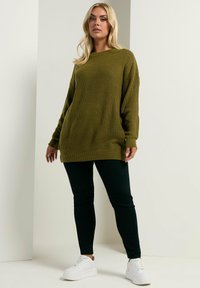 Un pull en laine vert olive à la coupe ample, texture côtelée et manches longues, associé à un pantalon slim noir et des baskets à plateforme blanches.