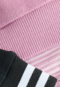 Trois échantillons de textile : un tricot lisse rose clair, un tricot ribbé gris foncé, et un motif rayé avec des bandes blanches et grises.