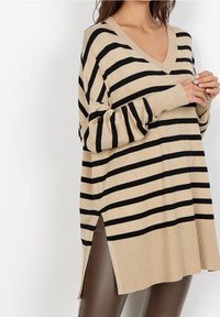 Beige gestreepte trui met zwarte horizontale strepen, V-hals, lange mouwen, zijsplitten en een ontspannen pasvorm, gemaakt van een zachte brei-stof.
