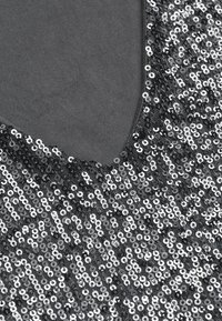 Svart paljetttyg med V-ringning, prytt med glänsande silverpaljetter arrangerade i ett enhetligt mönster på ett mjukt underliggande material.