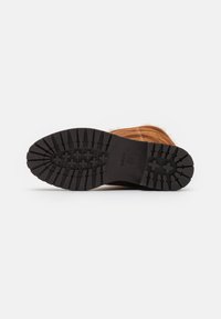 Stivale in suede marrone con una suola in gomma nera testurizzata, caratterizzato da motivi a rilievo profondi per una maggiore aderenza. L'altezza del tacco è moderata per il comfort.