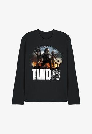 Drei entschlossene Personen mit Waffen stehen vor einem feurigen Hintergrund über dem Text "TWD 15" auf einem schwarzen Langarmshirt.