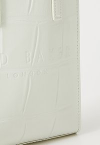 Weiße Kunstleder-Handtasche im Krokodil-Look mit eingeprägtem "DUNE BAKER LONDON"-Logo und kontrastierenden Nähten entlang der Kanten.
