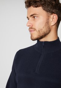 Navyblauer, zip-up Pullover mit einem strukturierten Streifenmuster. Hoher Kragen. Lockere Passform, warmes Material und klare Linien ohne Verzierungen.