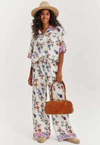 Květinový vzor, lehká látka, dvoudílná souprava v krémové barvě, skládající se z volného trička a širokých kalhot s barevnými akcenty. Součástí je hnědá kabelka.