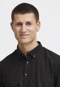 Camisa negra de botones con tejido texturizado y cuello, con botones en tono dorado y un peinado de corte corto.