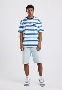 Striped T-shirt with blue and white colors, featuring a black “NYC” print. Worn with light denim shorts and sneakers.