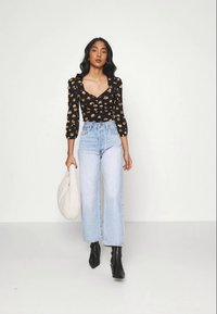 Zwarte bloemen lange mouw top met gerimpeld ontwerp, gecombineerd met hoog getailleerde lichtblauwe wijde jeans en zwarte enkellaarsjes. Houdt een witte tas vast.
