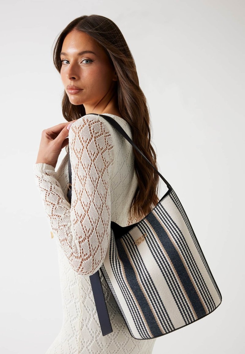 Borsa a secchiello in tela a righe beige, blu navy e pesca, con dettagli in pelle e una sola tracolla. Texture liscia con una forma strutturata.