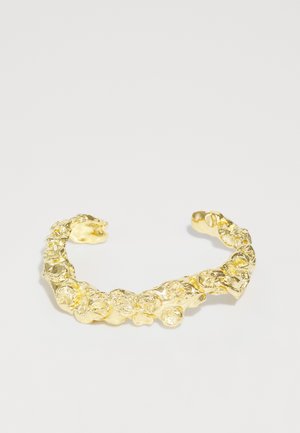 Zlatna manžetna narukvica s teksturiranim dizajnom koji sadrži organske, zaobljene oblike i nepravilne, uzdignute akcente diljem narukvice.