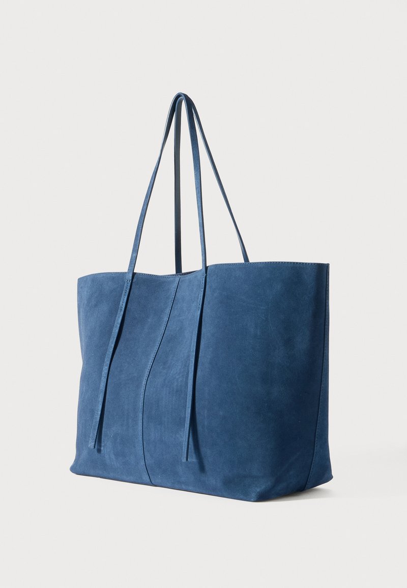 Borsa a tracolla in suede blu con due manici lunghi e piatti, caratterizzata da una texture liscia e dettagli di cuciture curve sul davanti.
