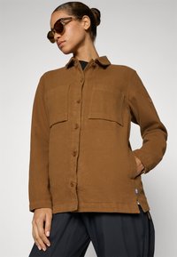 Bruine button-up jas met twee borstzakken, gemaakt van textuurstof, met een ronde kraag en subtiele logo-detail op de mouw.