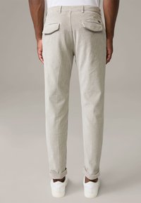 Pantalon en velours côtelé beige à coupe droite, avec deux poches arrière à rabats et revers retroussés, porté avec des baskets blanches.