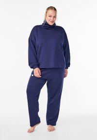 Navy blue loungewear set with a turtleneck top and elastic cuffs, paired with matching loose-fitting pants featuring a white accent.