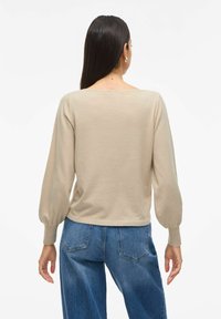 Beige gebreide trui met een diepe ronde halslijn en poffende lange mouwen, gecombineerd met blauwe denim hoge taillejeans. Zachte textuur en een ontspannen pasvorm.