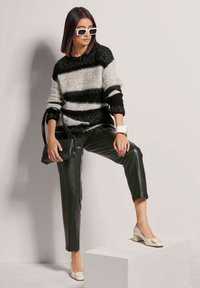 Gestreifter schwarz-weißer Strickpullover, schwarze Lederhose, weiße Blockabsatzschuhe und eine schwarze Handtasche mit einem strukturierten Design.