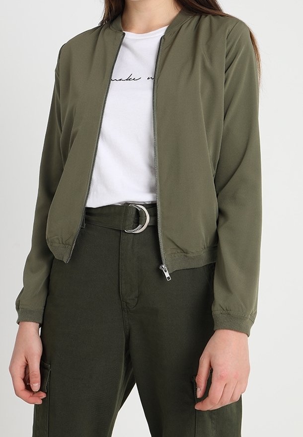 Blouson aviateur vert olive en tissu lisse, doté d'une fermeture éclair à l'avant, de poignets côtelés et d'une coupe ajustée, associé à un pantalon taille haute.