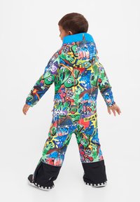 Färgglad snowsuit med graffiti-mönster, där huvan är blå, har långärmade ärmar och svarta muddar vid benen. Tillverkad av slitstarkt material.