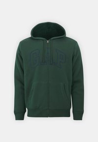 Sudadera verde con cremallera hecha de una tela suave, con un forro interior de felpa, bolsillos delanteros y el logo "GAP" en azul oscuro en el pecho.