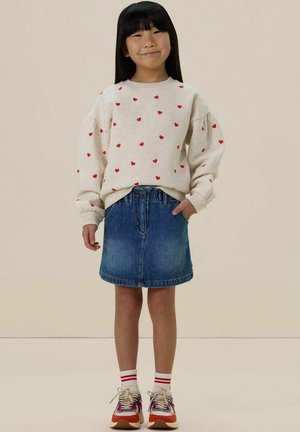 Hellgrauer Sweatshirt mit roten Herzmotiven, Jeansrock und mehrfarbigen Sneakern mit weißen gestreiften Socken. Lässiges Outfit, entspannter Schnitt.