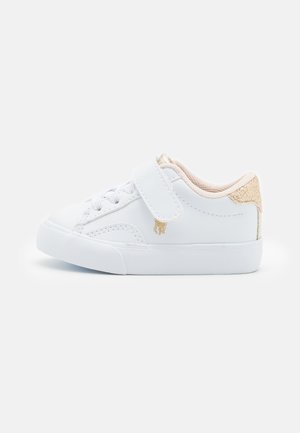 Bílé sneakers s texturovaným designem, vybavené suchým zipem a tkaničkami, s akcentem na zlacený třpytivý podpatek. Gumová podrážka, nízký profil.