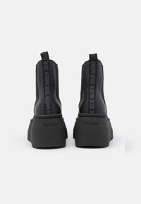 Stivaletti neri alla caviglia con finitura in pelle texturizzata, punta quadrata e suola platform spessa. Presentano un logo embossato sul tallone e dei tiranti.