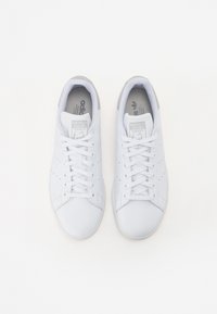 Hvide lædersneakers med perforerede sidedele, klassisk snøring og grå detaljer på hælen og tungen. Tekstureret gummisål.