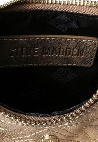 Zbliżenie na wnętrze torby z brązowej pikowanej skóry, z metalowym zamkiem błyskawicznym i skórzaną metką z wytłoczonym napisem "Steve Madden".