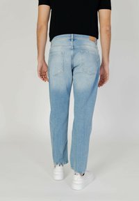 Jeans de denim azul claro con corte recto, lavado desvanecido y bolsillos traseros. Presenta un parche de cuero marrón claro en la cinturilla. Se combinan con zapatillas blancas.