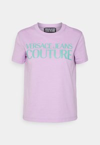 Lila kortärmad T-shirt med mintgrön "VERSACE JEANS COUTURE" text på framsidan och en svart etikett inuti kragen.