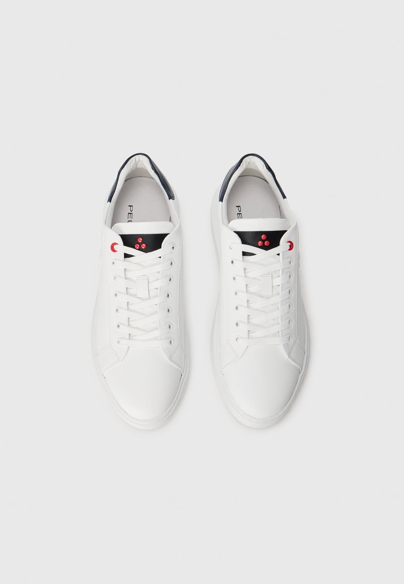 Un paio di sneaker bianche basse con lingua nera, occhielli rossi e logo a pois rossi su sfondo bianco, viste dall'alto.