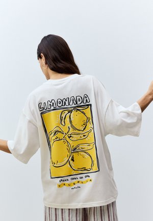 Fehér, túlméretezett póló sárga citrom grafikával a hátoldalon, fekete körvonalakkal és a "LIMONADA VALENCIA ESPAÑA" felirattal.