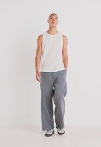 Hvit ribbestrikket tanktop og løse grå joggebukser. Antrekket har myk stoff med subtil tekstur, komplementert av grå fottøy.