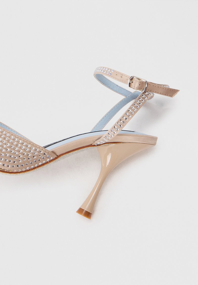 Sandale à talon haut beige avec un design clouté, une bride de cheville et un talon effilé brillant. L'intérieur présente des accents bleu clair.