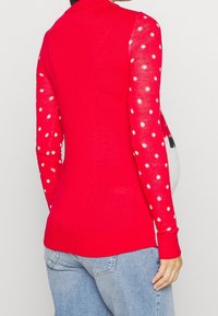 Roter Pullover mit langen Ärmeln und weißen Punkten. Strickstruktur mit figurbetontem Design, geripptem Ausschnitt und Bündchen.